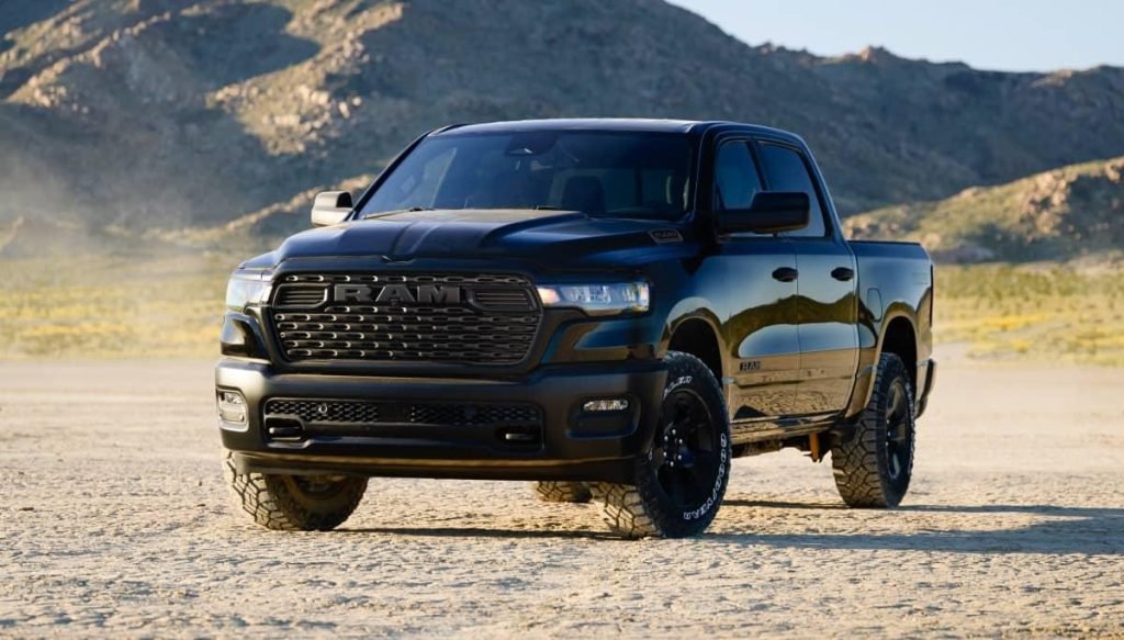 A black pickup truck is parked on a flat, sandy area with rugged mountains in the background under a clear sky.