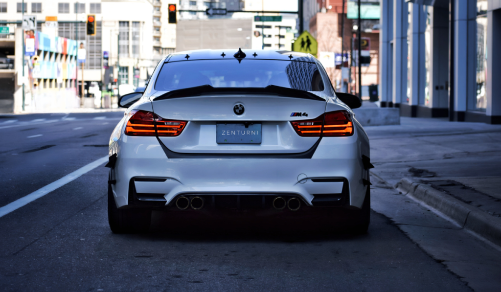 A white BMW M4 with tinted windows and a custom license plate reading “ZENTURNI” is parked on a city street near modern buildings, showcasing the sleek look achievable after a professional Chandler windshield replacement.