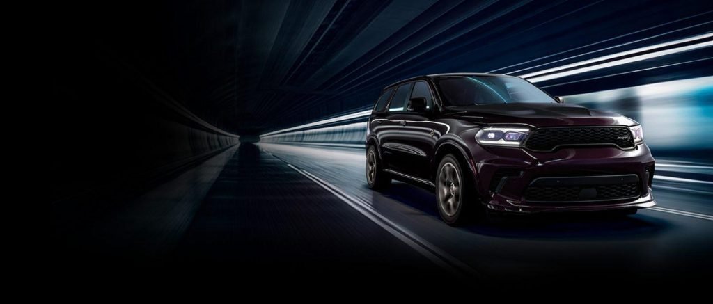 A dark SUV drives through a futuristic illuminated tunnel with blurred blue and white light streaks.