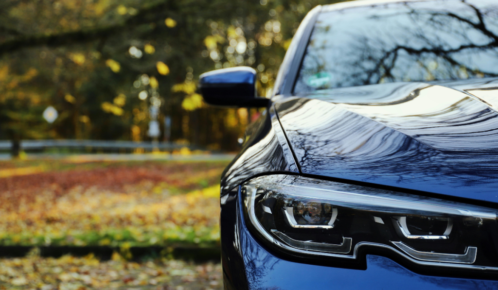 Close-up of the front right side of a shiny blue car with modern headlights, parked outdoors on an autumn day with trees and fallen leaves—perfect for showcasing chandler windshield replacement quality.