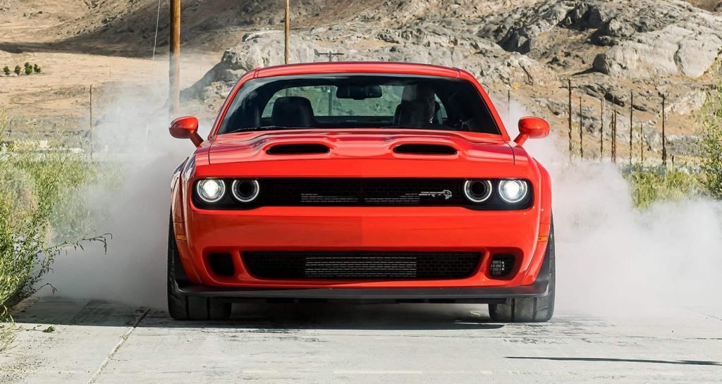 A red muscle car performs a burnout on a rural road, smoke billowing from the rear tires in dramatic style.