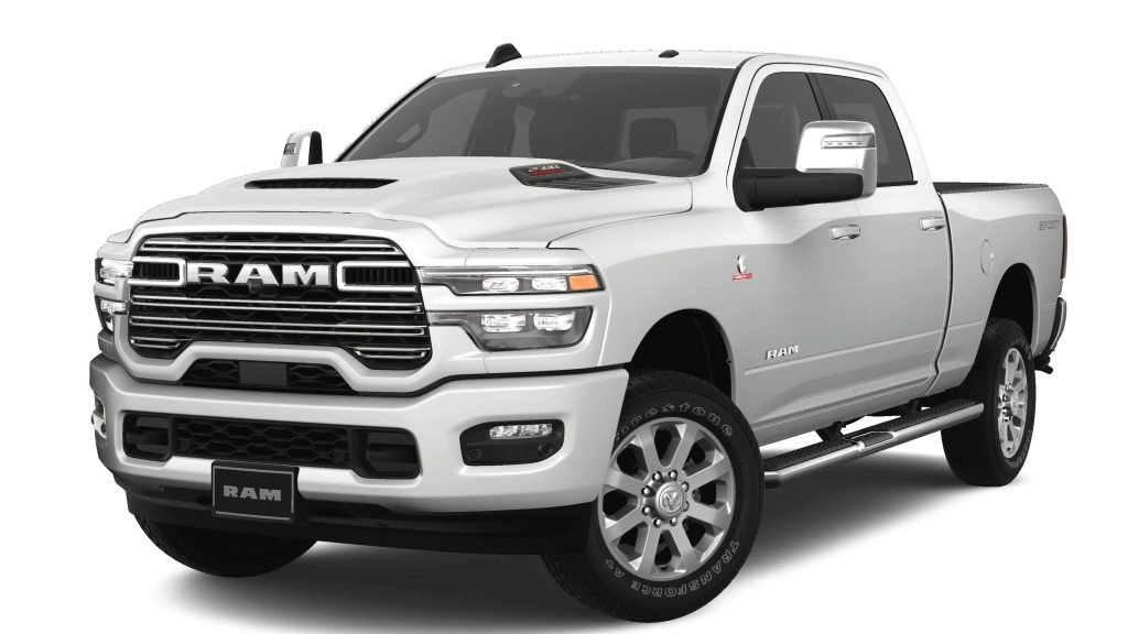 A white Ram pickup truck viewed from the front and side, showcasing its bold grille, large headlights, four doors, rugged tires, and chrome detailing. The truck is parked on a plain white background.