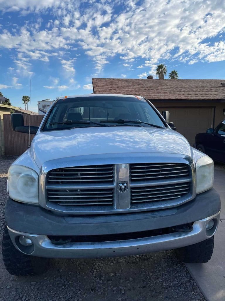 A white Dodge pickup truck is parked on a driveway outside a house beneath a partly cloudy sky.