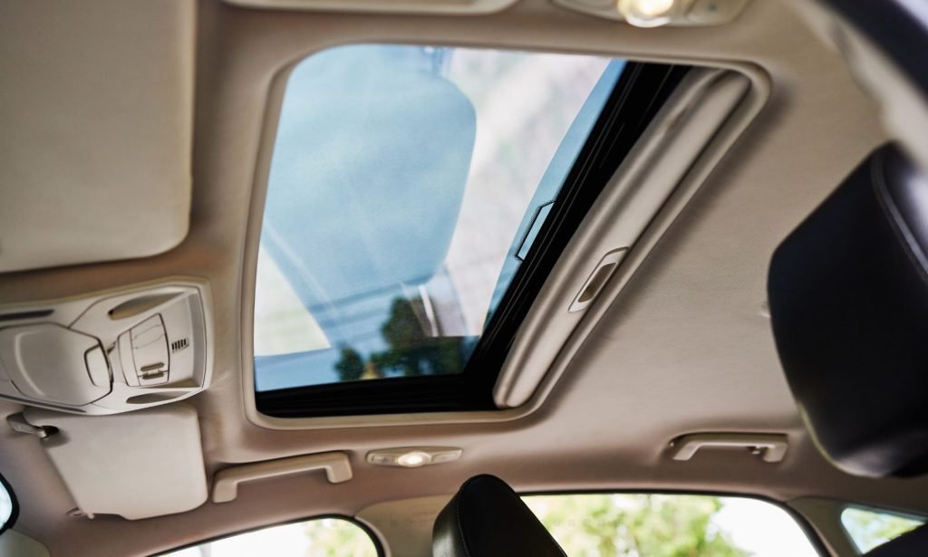 Interior view of a car sunroof, highlighting the glass panel, beige car interior, and front seat.