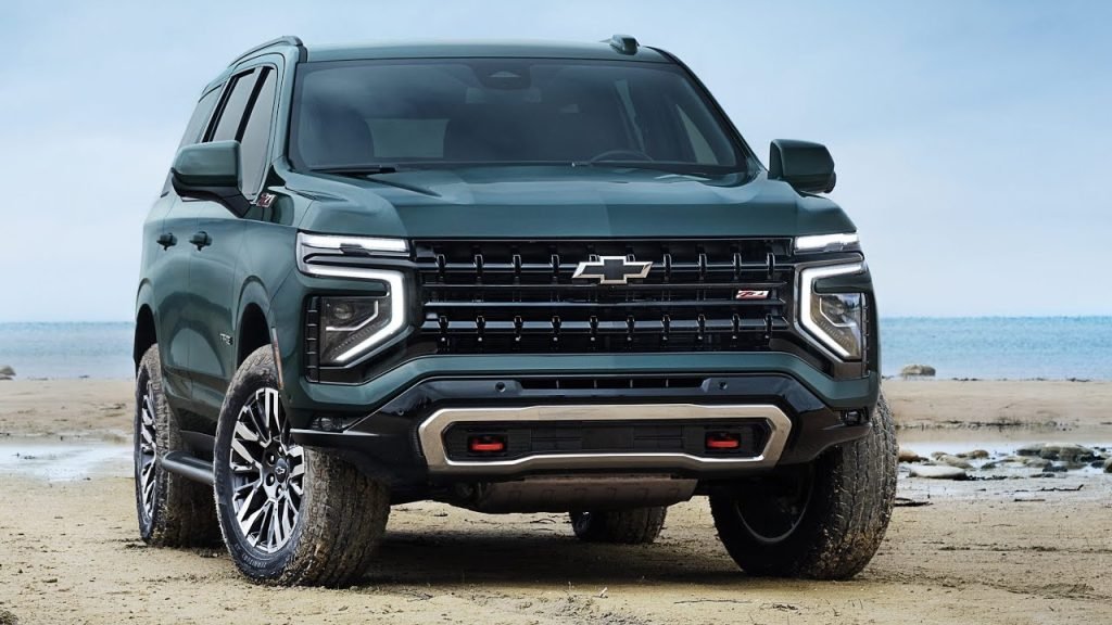 A green Chevrolet SUV with bold LED headlights and a prominent grille is parked on a sandy beach with the ocean in the background under a cloudy sky.