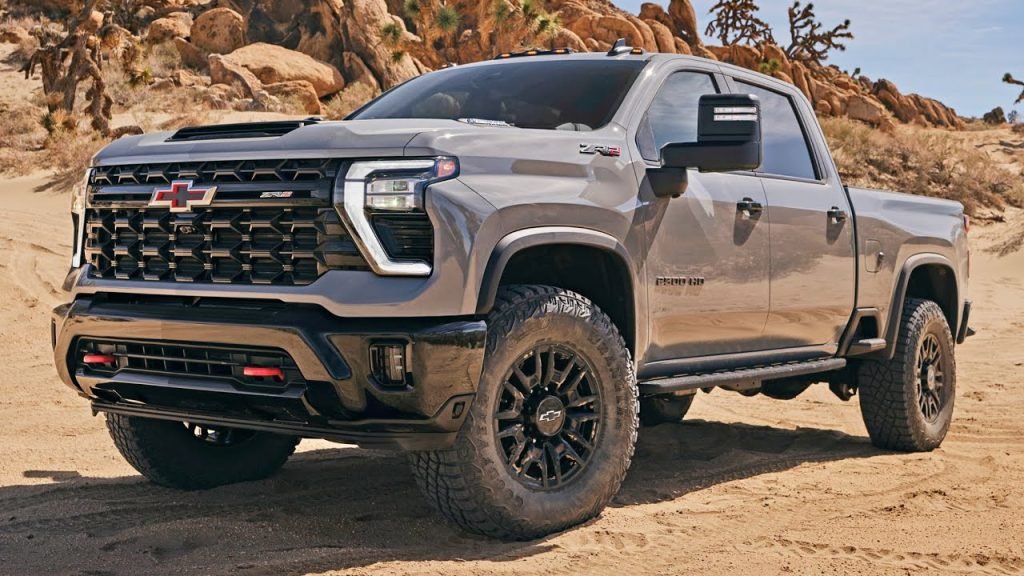 A gray Chevrolet Silverado ZR2 pickup truck is parked on sandy terrain with rocks and sparse desert vegetation in the background.