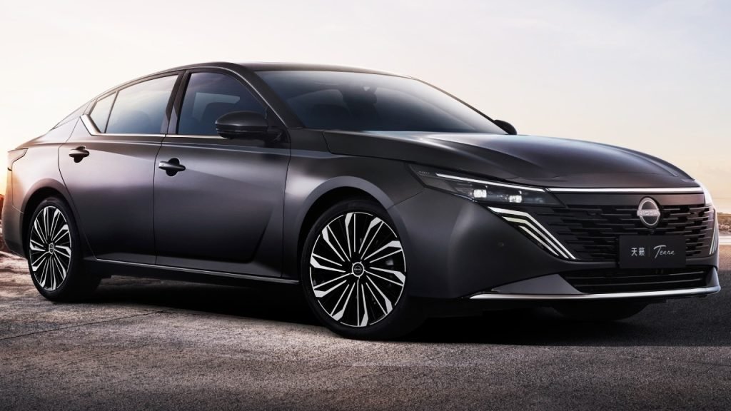 A sleek, modern black sedan with sharp lines and stylish alloy wheels is parked outdoors on a paved surface at sunset. The car features slim LED headlights and a distinctive front grille design.